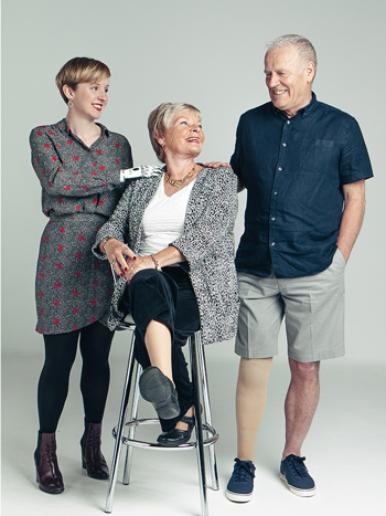 Three smiling amputees wearing their prosthetic devices, two women one man, with one woman sat on a stool