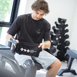 Adult male with right arm and right leg Prosthetic devices for limb difference sat in a clinic gym room holding a towel above prosthetic leg socket